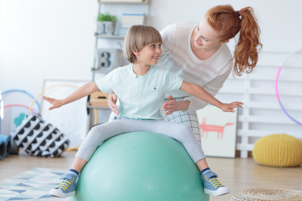 Physical,Therapist,Assisting,Little,Boy,Sitting,On,Gym,Ball,During